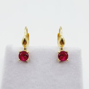 May include: A pair of gold earrings with a small, round, red gemstone hanging from each.