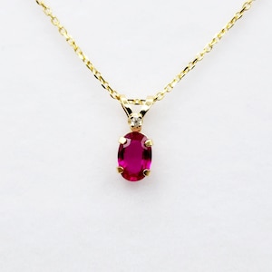 May include: A gold chain necklace with a pendant featuring a large oval-shaped ruby gemstone and a smaller diamond accent.