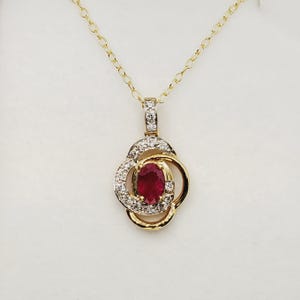 Può includere: Una collana dorata con un pendente con un rubino ovale centrale circondato da piccoli diamanti. Il pendente ha un design floreale con una catena delicata. Il rubino è di un rosso intenso e i diamanti brillano.