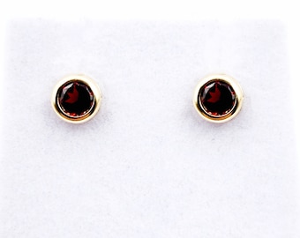 May include: A pair of gold stud earrings with small, round, red gemstones.