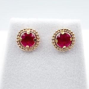 May include: A pair of gold earrings with red ruby gemstones set in a beaded halo design.