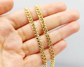 May include: Two gold chains, one on top of the other, are shown in a hand. The chains are made of a thick, curb link design.