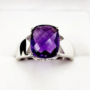 May include: A silver ring with a large, faceted amethyst gemstone. The ring has a simple band and a bezel setting.