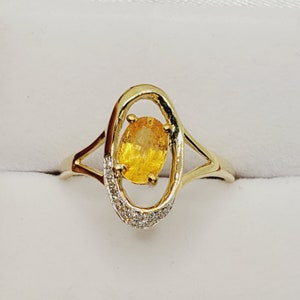 May include: A gold ring with a yellow oval gemstone set in a delicate oval frame. The frame is accented with small diamonds.