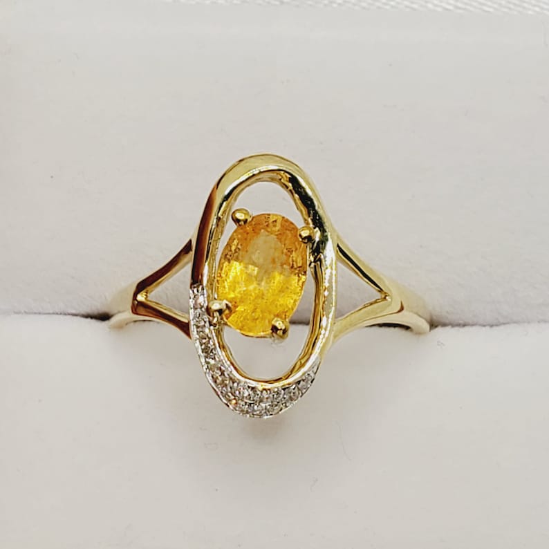 May include: A gold ring with a yellow oval gemstone set in a delicate oval frame. The frame is accented with small diamonds.