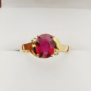 May include: A gold ring featuring a large oval ruby gemstone and two smaller diamond accents.