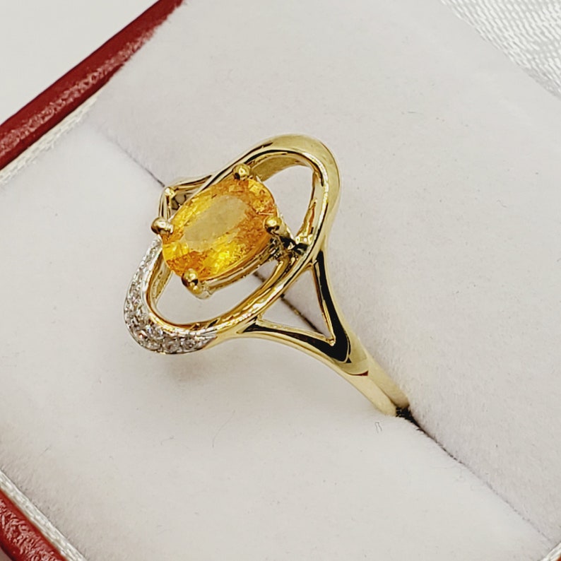 May include: A gold ring with a large oval-shaped yellow gemstone set in a delicate, open-work design. The ring is accented with small, sparkling diamonds.