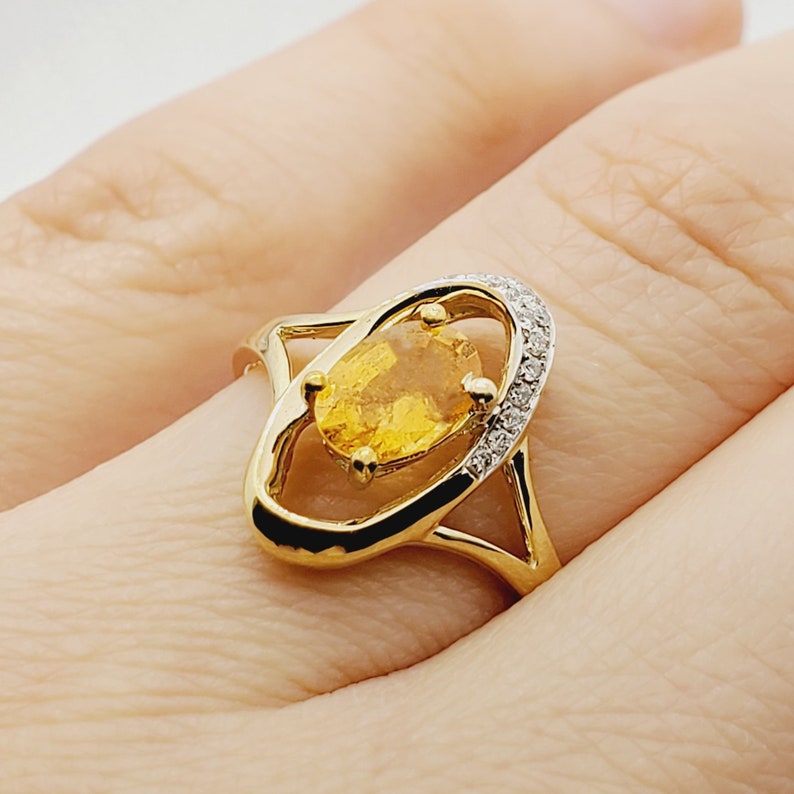 May include: A gold ring with a large oval-shaped yellow gemstone surrounded by a halo of smaller diamonds.