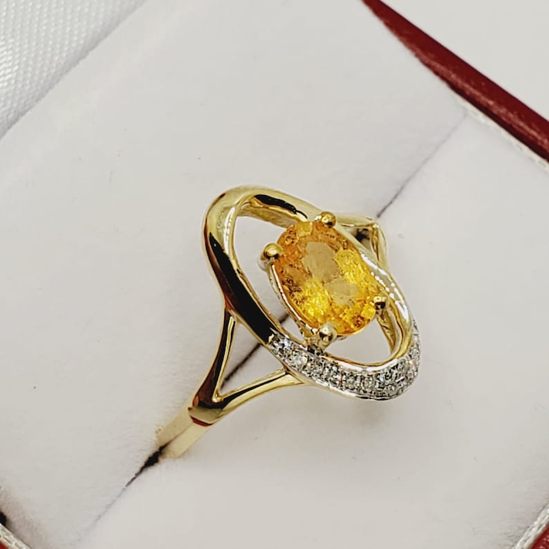 May include: A gold ring with a large oval-shaped yellow gemstone surrounded by a halo of smaller diamonds.