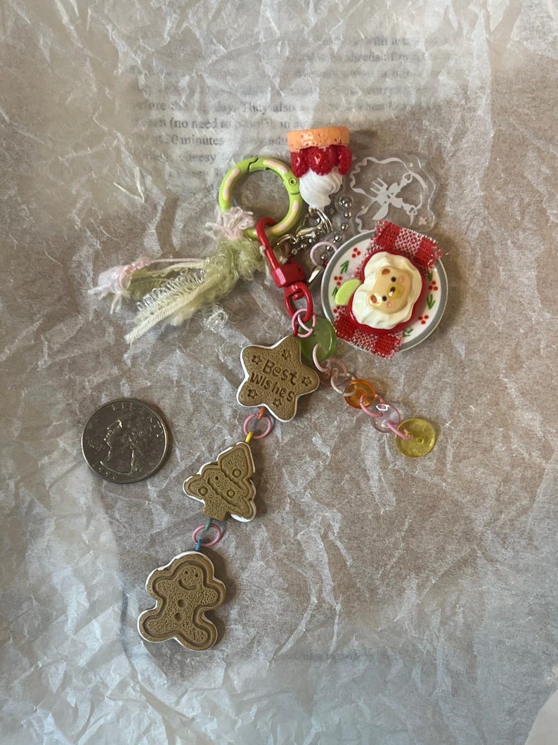 K&ouml;nnte beinhalten: Ein farbenfrohes Charm-Armband mit einem Lebkuchenmann, einem Weihnachtsbaum, einem Stern mit der Aufschrift "Beste W&uuml;nsche" und einem Teller mit einem b&auml;renf&ouml;rmigen Kuchen. Das Armband enth&auml;lt auch ein rot-wei&szlig;es Karomuster, einen gr&uuml;nen Ring und einen rot-wei&szlig;en Erdbeerkuchen.