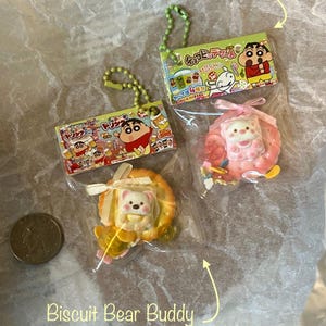K&ouml;nnte beinhalten: Zwei kleine, bunte Plastik-Anh&auml;nger mit Schl&uuml;sselringen. Ein Anh&auml;nger ist ein rosa-wei&szlig;es Schwein mit einer gelben Schleife. Der andere Anh&auml;nger ist ein gelber B&auml;r mit einer wei&szlig;en Schleife. Beide Anh&auml;nger befinden sich in einer durchsichtigen Plastikverpackung mit japanischem Text.