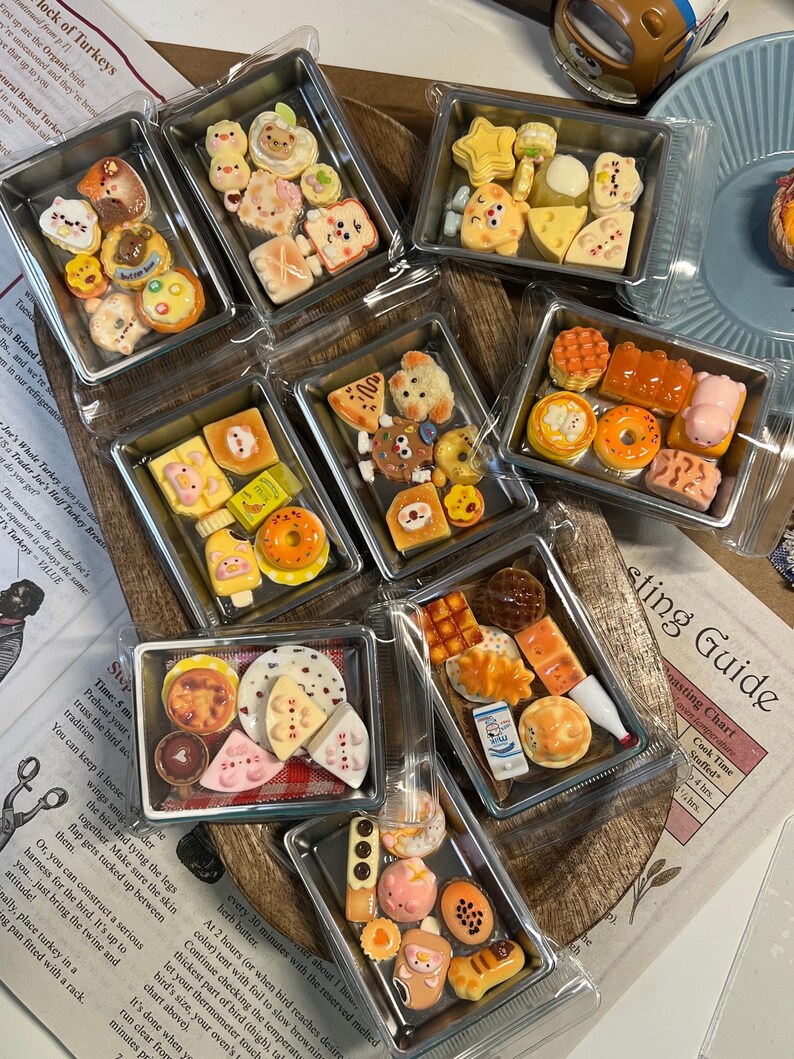 May include: A collection of miniature food items, including pastries, fruits, and other treats, arranged in clear plastic containers. The food items are brightly colored and detailed, with various shapes and designs. The image is taken from above.