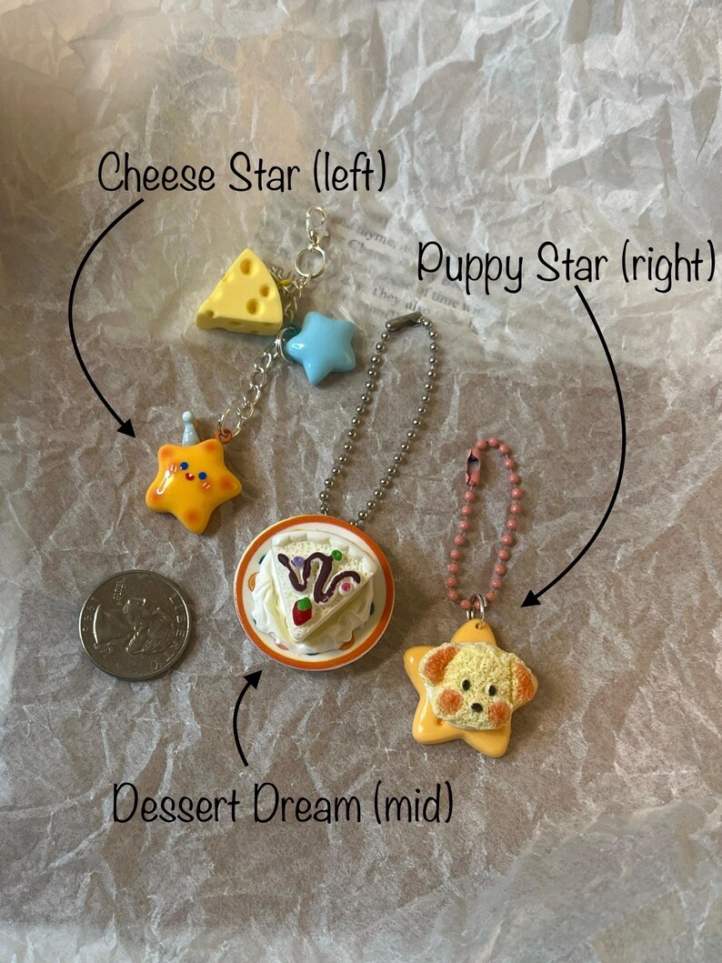 K&ouml;nnte beinhalten: Drei bunte Gl&uuml;cksbringer-Halsketten mit verschiedenen Motiven: ein St&uuml;ck K&auml;se, ein blauer Stern und ein gelber Stern mit einem Gesicht; ein St&uuml;ck Kuchen auf einem Teller; und ein gelber Stern mit einem Hundefoto.