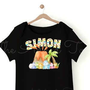 K&ouml;nnte beinhalten: Schwarzer Baby-Strampler mit einem bunten Vulkandesign und dem Namen "SIMON" darauf gedruckt. Der Vulkan hat einen Palmenbaum und Comic-Dinosaurier drumherum.