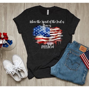 May include: A black t-shirt with a watercolor American flag design and the text "Where the Spirit of the Lord is there is FREEDOM".