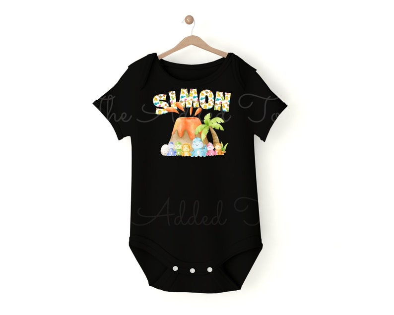 K&ouml;nnte beinhalten: Schwarzer Baby-Strampler mit einem bunten Vulkandesign und dem Namen "SIMON" darauf gedruckt. Der Vulkan hat einen Palmenbaum und Comic-Dinosaurier drumherum.