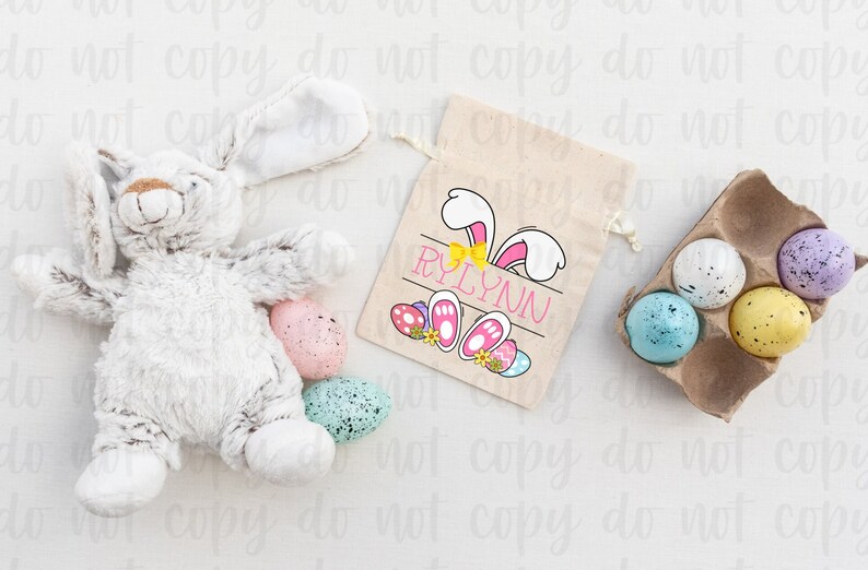 May include: A white bunny-shaped Easter gift bag with a pink bunny design and the name "RYLYNN" printed on it. The bag is filled with colorful Easter eggs.