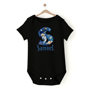 May include: Black baby onesie with a blue and white astronaut graphic in the shape of the letter S. The onesie has the name "Samuel" printed below the graphic.