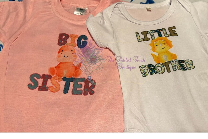 May include: Two infant shirts, one pink and one white, with a dinosaur and a lion graphic. The pink shirt says "Big Sister" and the white shirt says "Little Brother".