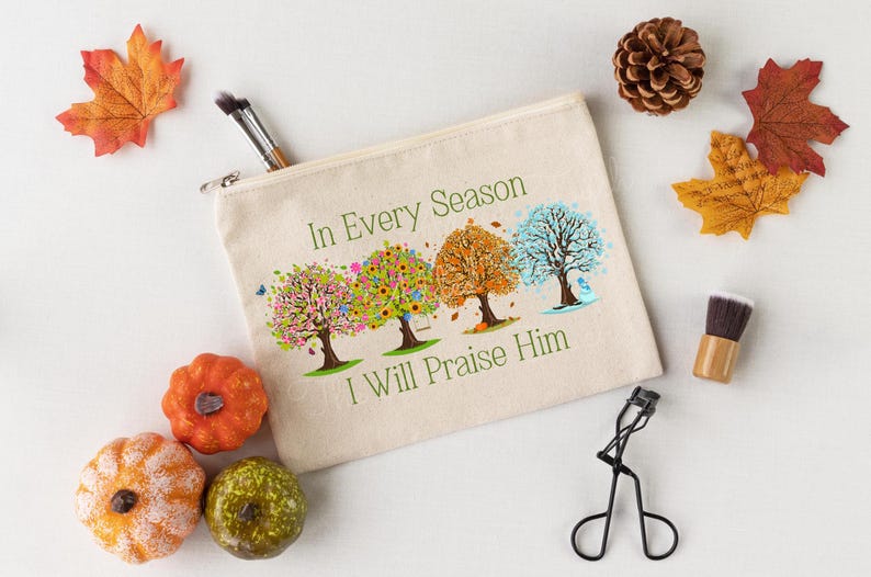 May include: A white canvas zippered pouch with a colorful design of four trees representing the four seasons. The text "In Every Season I Will Praise Him" is printed on the pouch.