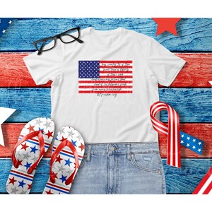 May include: White t-shirt with a red, white, and blue American flag graphic and text that reads "My Country, 'Tis of Thee, Sweet Land of Liberty, Of Thee I Sing."