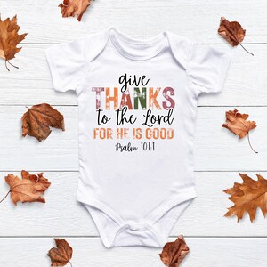 May include: White baby onesie with the text "give thanks to the Lord for he is good Psalm 101:1" in colorful, distressed lettering.