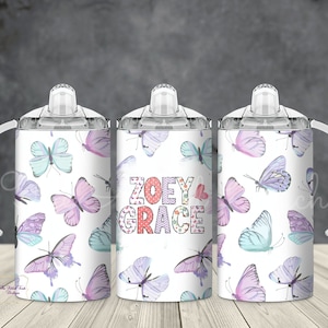 May include: Three white stainless steel cups with clear lids and handles. The cups have a butterfly pattern with pink, purple, and blue butterflies. The middle cup has the names "ZOEY & GRACE" in pink, red, and white letters.