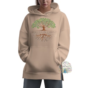 Peut inclure: Un sweat &agrave; capuche beige avec un motif d'arbre avec des racines et le texte "Rooted in Christ".