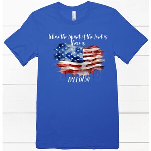 May include: A royal blue t-shirt with a watercolor American flag design. The text "Where the Spirit of the Lord is there is FREEDOM" is printed on the shirt.
