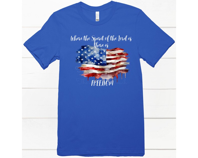 May include: A royal blue t-shirt with a watercolor American flag design. The text "Where the Spirit of the Lord is there is FREEDOM" is printed on the shirt.