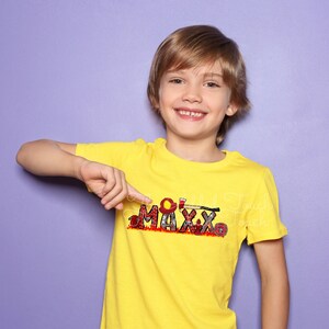 May include: A young boy wearing a yellow t-shirt with a firefighter themed design that says "MAXX" in red, black, and white. The design includes a fire helmet, axe, and hose.