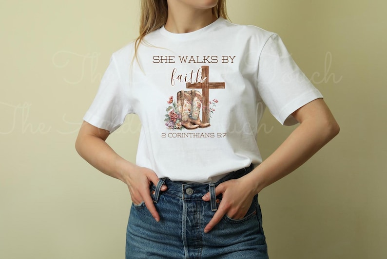 May include: White t-shirt with the text "She walks by faith" and a pair of brown cowboy boots with a cross behind them. The text "2 Corinthians 5:7" is below the boots.