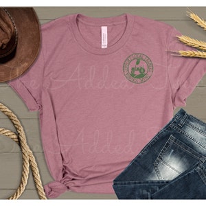 Pu&ograve; includere: Una maglietta color malva con una grafica verde di un trattore e il testo "Support Local Farmers Virginia, West Virginia".