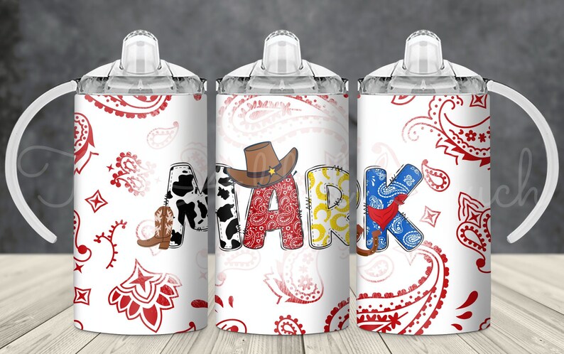 May include: Three white tumblers with red and white paisley patterns. The tumblers have clear lids and handles. The middle tumbler has the name "MARK" spelled out in colorful letters with cowboy-themed embellishments.