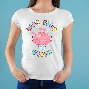 May include: White t-shirt with a pink cartoon brain wearing glasses and holding its hands up. The text "Kiss Your Brain" is written in rainbow colors above the brain.