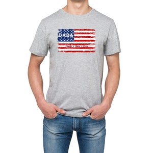 May include: A gray t-shirt with a distressed American flag design. The flag has the word "DADA" in blue letters and the words "Charlie, Claire & Cyrus" in smaller blue letters below the flag.