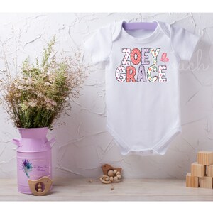 May include: White baby onesie with the names "ZOEY GRACE" in colorful patterned letters. A pink butterfly is next to the names.