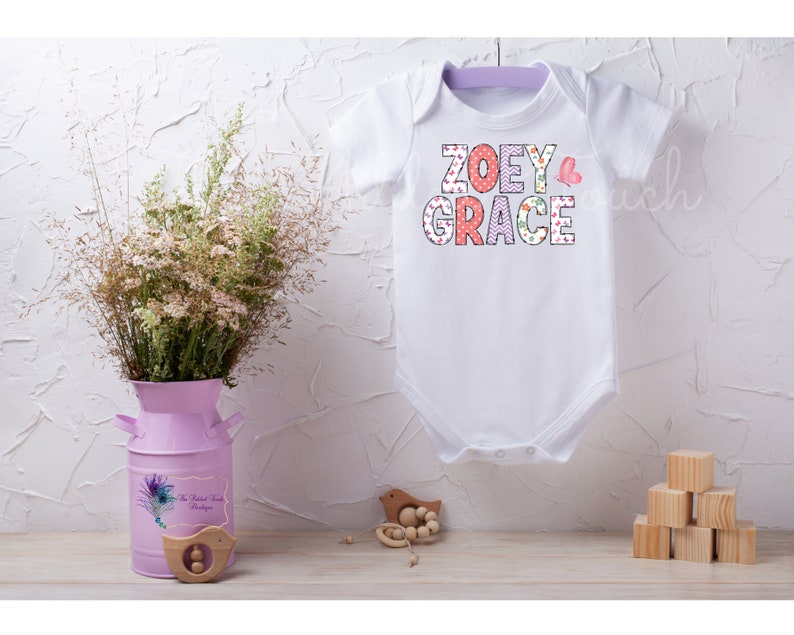 May include: White baby onesie with the names "ZOEY GRACE" in colorful patterned letters. A pink butterfly is next to the names.