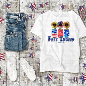 May include: White t-shirt featuring a design of three mason jars decorated with red, white and blue stars and sunflowers. The text "Free Indeed" and "John 8:36" is printed below the jars.