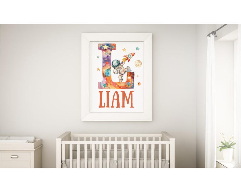 May include: A white framed print with a watercolor illustration of a letter L with an astronaut in a space suit holding a rocket. The letter L is filled with a galaxy design and the name Liam is printed below the letter.