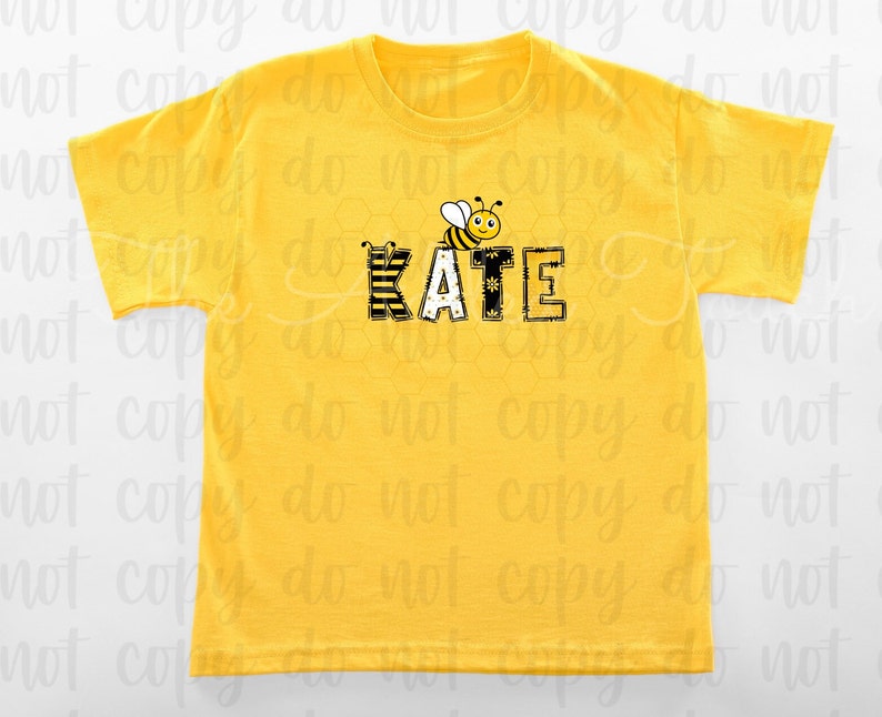 May include: Yellow short-sleeved t-shirt with a black and yellow bee graphic and the name "KATE" in black letters with a yellow and black striped pattern.