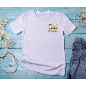 May include: White t-shirt with the text "First Grade" in yellow and black letters, with the words "Glowfire Elementary" underneath.