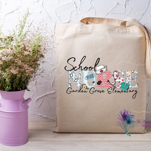 May include: A beige canvas tote bag with the text "School Nurse Garden Grove Elementary" printed on it. The letters are decorated with colorful medical-themed patterns.