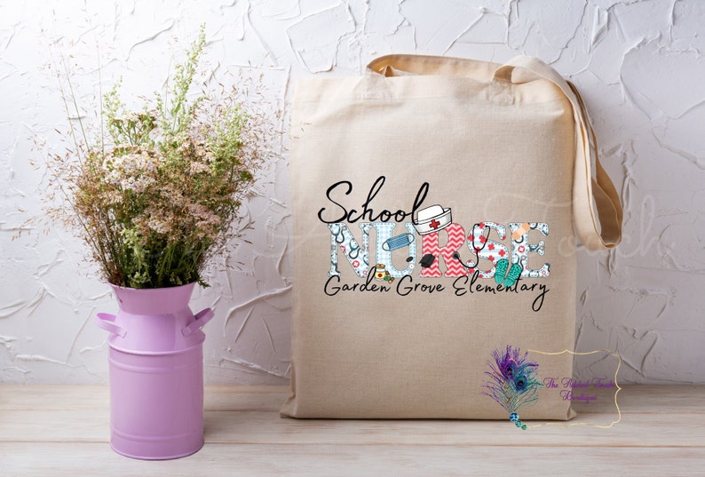 May include: A beige canvas tote bag with the text "School Nurse Garden Grove Elementary" printed on it. The letters are decorated with colorful medical-themed patterns.