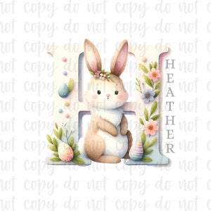 May include: A white letter H with a light blue background. A brown bunny with a pink nose and white whiskers is standing next to the letter. The bunny is wearing a flower crown. The letter is decorated with pink, purple, and white flowers. The word "HEATHER" is written vertically on the right side of the letter.
