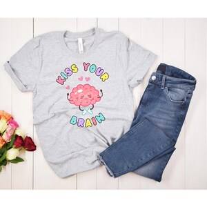 May include: A gray t-shirt with a pink brain cartoon wearing glasses and the text "Kiss Your Brain" in rainbow colors.