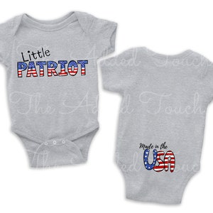 May include: A grey baby onesie with the text "Little PATRIOT" in red, white and blue on the front. The back of the onesie has the text "Made in the USA" in red, white and blue.