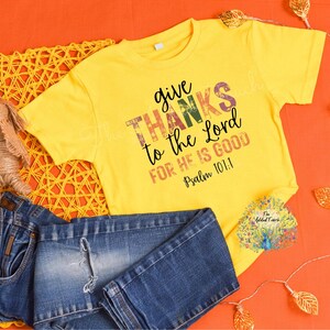 May include: Yellow short-sleeved t-shirt with a distressed graphic print that says "give thanks to the Lord for He is good Psalm 101:1".