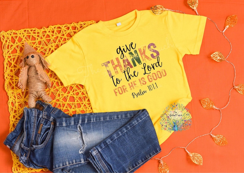 May include: Yellow short-sleeved t-shirt with a distressed graphic print that says "give thanks to the Lord for He is good Psalm 101:1".
