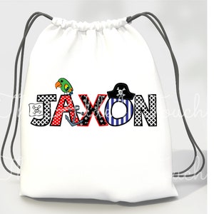 May include: White drawstring bag with a pirate-themed design featuring the name "Jaxon" in colorful letters with a parrot, anchor, and pirate hat.